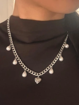 Silvrigt halsband, 6 mm brett med hjärthänge - Matchande örhängen finns i en separat annons. Finns även i guldpläterad variant.  Material: Rostfritt stål Bredd: 6 mm Längd: 42 + 8 cm (justerbar) Övrigt: Nickelfritt och handgjort