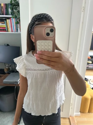 Vit blus med spets från H&M Divided - Supersöt vit blus från H&M Divided i storlek M. Blusen har korta volangärmar, spetsdetalj över bröstet och är gjord i ett lätt, krinklat bomullstyg. Perfekt till sommaren och enkel att styla med jeans eller kjol. Nästan aldrig använd och liten i storleken!