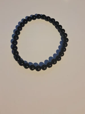 Svart pärlarmband obsidian - Snyggt svart armband med runda pärlor trädda på elastisk tråd. Perfekt accessoar för att ge din outfit en stilren touch. Passar både ensam eller i kombination med andra armband.