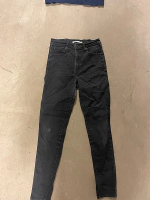 Svarta skinny jeans från Levi's - Säljer ett par svarta skinny jeans från Levi's med klassisk femficksdesign och hög midja. Jeansen har en smal passform och är tillverkade i stretchigt denimtyg för extra komfort. Perfekta till en avslappnad streetstyle-look.
