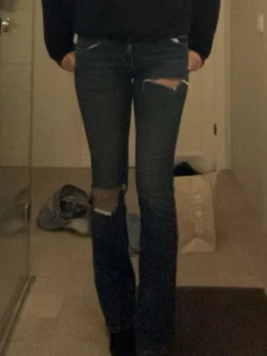 Mörkblå bootcut jeans - Säljer ett par mörkblå bootcut jeans med stora slitningar över knäna och låren. De är från Zara. Skitsnygga men lite för korta för mig som är 170