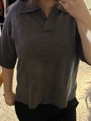 Casemir  Grå polotopp med krage - Mysig grå polotopp med krage och halv djup v-ringning. Toppen har halvlånga ärmar och en loose passform som ger en avslappnad vibe. Perfekt att styla med jeans eller kjol för en enkel men snygg look.