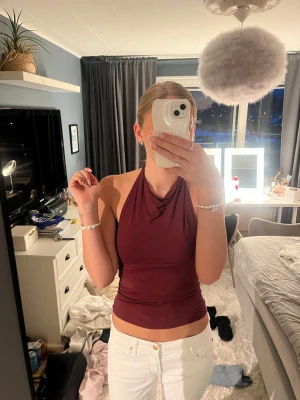 Vinröd halterneck topp - Säljer en vinröd halterneck topp med öppen rygg och croppad passform. Toppen har en snygg drapering framtill och är perfekt för dig som vill ha en trendig och stilren look. Materialet känns mjukt och stretchigt.