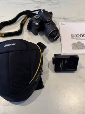 Nikon D3200 systemkamera med tillbehör - Säljer en svart Nikon D3200 systemkamera med AF-S DX NIKKOR 18-55mm objektiv. Medföljer originalkamerarem, svart Nikon-väska med gul detalj, batteriladdare och användarmanual. Perfekt för dig som vill ta snygga bilder och utveckla ditt fotograferande.