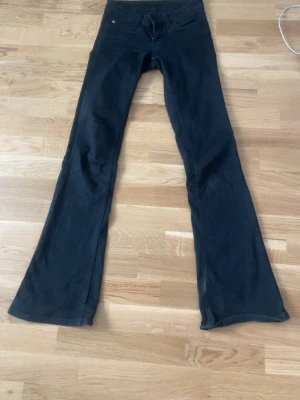 Svarta bootcut jeans - Säljer ett par svarta bootcut jeans med klassisk femficksdesign och låg midja. Jeansen har utsvängda ben och är tillverkade i ett mjukt denimtyg som ger en skön passform. Dem är köpta på WEEKDAY för 4 månader sen