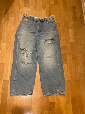 Blåa baggy ripped jeans zara  - Säljer ett par ljusblå baggy jeans med slitna detaljer och stora hål på benen. Jeansen har hög midja, fem fickor och raka ben. Perfekta för en avslappnad och trendig streetstyle-look. Materialet är klassisk denim i bomull. storlek 42 nypris 499kr slutsåld viral modell 
