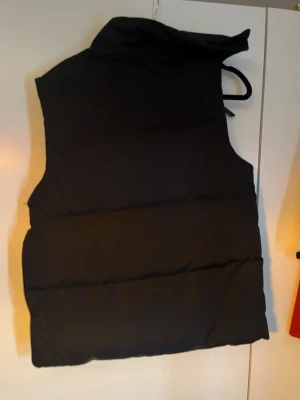 Svart dunväst från Hoodrich - Snygg svart dunväst från Hoodrich med stor ficka framtill och tryckt logga på bröstet. Västen har hög krage och texten 'FROM NOTHING TO SOMETHING' nedtill. Perfekt för lager på lager och streetwear-stil.