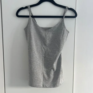 Grått linne - Säljer en enkel och stilren grå linnetopp från lager157 med smala axelband och v-ringning. Perfekt att matcha med jeans eller kjol för en avslappnad look. Materialet är mjukt och stretchigt, vilket gör den bekväm att bära hela dagen.