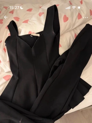 Set från Zara - Säljer en svart jumpsuit från Zara med breda axelband och figurnära passform. Plagget har en elegant skärning vid halsen och långa byxben. Perfekt för dig som gillar stilrena och trendiga plagg. Materialet är mjukt och följsamt.