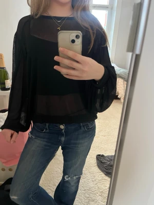 Svart transparent blus med vida ärmar - Säljer en svart transparent blus med vida, långa ärmar och lös passform. Blusen har en rund halsringning och är tillverkad i ett lätt, tunt material som ger en luftig känsla. Har även en tråd som man kan knyta baktill för att bestämma ”kortleken” på tröja💞