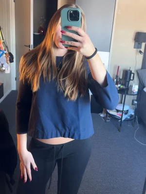 Mörkblå croppad topp med slits bak - Trendig mörkblå croppad topp med trekvartsärm och slits baktill. Säljer då den börjar bli för liten och inte kommer till användning. 