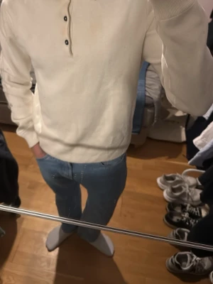 Vit stickad pikétröja Bondelid - Vit stickad pikétröja från Bondelid med klassisk krage och tre svarta knappar framtill. Tröjan har lång ärm och ribbade muddar vid ärmslut och nederkant. Perfekt för en clean och stilren look.