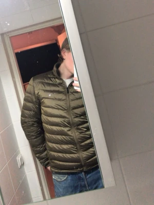 Olivgrön gant dunjacka med hög krage - Säljer en olivgrön dunjacka med quiltad design och hög krage. Jackan har dragkedja framtill och två sidofickor. Lätt och smidig modell som håller värmen bra under kalla dagar. Perfekt för vintern och enkel att matcha med olika outfits. Fick fel storlek när jag beställde denna så den har inte kommit till användning! 