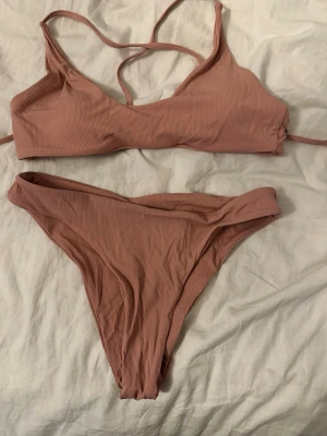 Rosa ribbad bikini med smala band - Trendig rosa bikini med ribbad struktur och smala axelband. Överdelen har enkel design med vaddering och underdelen är högt skuren för en modern look. Perfekt för stranddagar eller poolhäng.