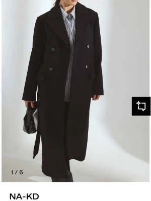 Svart lång kappa från NA-KD - Stilren svart lång kappa från NA-KD med dubbelknäppning. Helt ny o använd 1 gång! Vill ha en större storlek men då jag använt den går de inte att skicka tillbaka