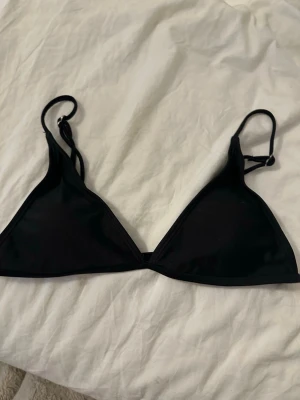 Svart trekantsbikinitopp - En enkel och stilren svart trekantsbikinitopp med tunna axelband och justerbar knytning i ryggen. Perfekt för lata dagar på stranden eller vid poolen. Klassisk modell som passar till det mesta.