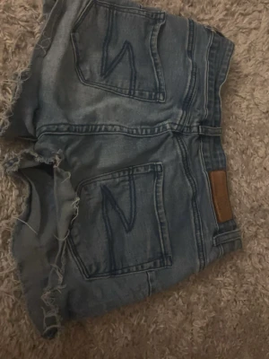 Blå jeansshorts från Zara - Säljer ett par blå jeansshorts från Zara med råa, fransiga kanter och klassiska bakfickor. Shortsen är lågmidjade och går att göra mer lågmidjande om man bokar in där uppe, jätte snygga har dock växt ur och vill sälja 
