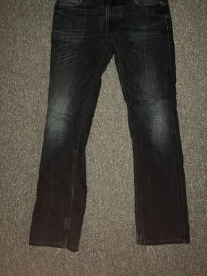 Nudie thin finn - Säljer ett par svarta/mörkblå, slim/straight fit jeans med snygga slitningar och tvättade detaljer. Jeansen har fem fickor och klassisk knappgylf. Materialet är denim med en skön känsla. Byxorna är storlek w32 l32 men passar som ~ w29 l31, Har du några frågor är det bara att skriva🙌