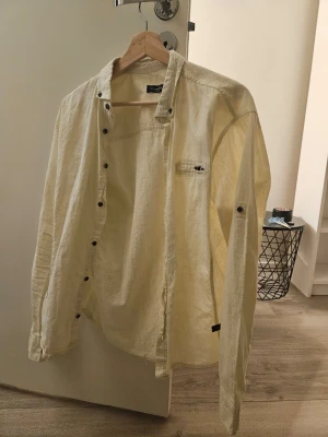 NY gul skjorta - Säljer en ny gul skjorta, aldrig använd, bara etiketten är borttagen i mjukt bomullsmaterial. Skjortan har knappar längs bröstet, en liten bröstficka med dragkedja och avslappnad passform. Storleken på etiketten är XL, men enligt min mening passar den bättre för storlek L.