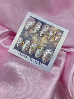 AngelGlaze (S);Short Almond - Unika handgjorda press-on naglar i pärlemorvit med skimrande finish och 3D-effekt. Dekorerade med små guldfärgade detaljer och stjärnor. Korta/Mandelformade och handgjorda för en exklusiv look. Perfekta för dig som vill sticka ut med trendiga naglar.S: 15 mm, 11,5 mm, 12 mm, 11 mm, 9 mm 