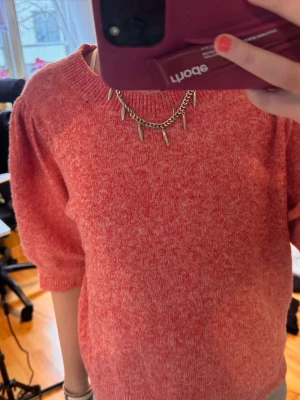 Rosa stickad tröja med puffärm - Mysig rosa stickad tröja med korta puffärmar och rund halsringning. Tröjan har en melerad struktur och ribbstickade muddar vid ärmslut och nederkant. Perfekt för lager-på-lager och en avslappnad stil.