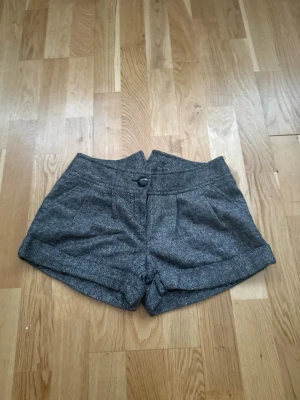 Grå eleganta shorts - Snygga grå shorts i ett elegant tyg med klassisk design. Perfekta både till vardag och lite mer uppklätt tillfälle.  Shortsen har låg midja, dekorativ knapp framtill och en stilren passform. Lätta att matcha med topp, skjorta eller kavaj.  Bra skick.