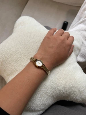 Elegant guldfärgad klocka, justerbar - Säljer en stilren guldfärgad klocka med klassiskt runt ur och vit urtavla. Armbandet är metall och har en snygg länkdesign som ger ett lyxigt intryck. Perfekt för dig som vill ha en tidlös accessoar som lyfter din outfit.