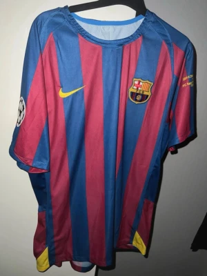 Barcelona matchtröja Nike blå/röd - Säljer en officiell FC Barcelona matchtröja från Nike med blå och röda vertikala ränder. Tröjan har klubbmärke på bröstet, Champions League-märke på ärmen och gula detaljer. Tillverkad i lätt och ventilerande material, perfekt för fotboll eller träning. pris kan diskuteras 