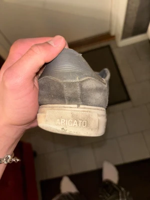 Grå sneakers från Axel Arigato - Snygga grå sneakers från Axel Arigato med klassisk låg profil och vita sulor. Skorna har en stilren design med matchande grå skosnören och diskret logga på hälen. Tillverkade i läder för en clean och modern look.