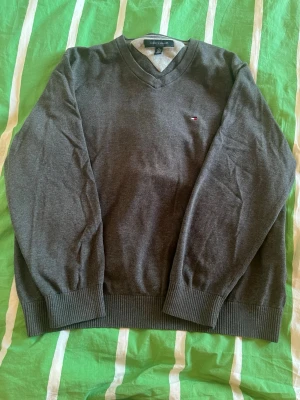 Tommy Hilfiger tröja XL - Snygg mörkgrå V-ringad tröja från Tommy Hilfiger. Tröjan har ett litet hål på baksida arm men som inte syns om man inte kollar väldigt noga. Strl XL