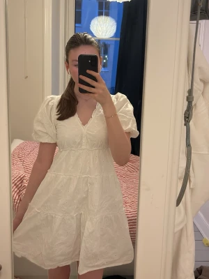 Vit sommrig klänning från Cubus  - Söt vit sommar klänning med puffärmar och v-ringning. Klänningen har broderade detaljer och en luftig, volangig kjol. Perfekt för sommarens alla tillfällen och ger en romantisk vibe. Tillverkad i bomull för en skön och sval känsla.