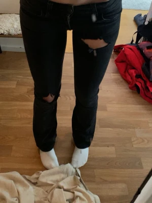 Low waist Svarta slitna jeans med hål - Säljer ett par low waist svarta jeans med trendiga hål på låret och knät. Jeansen har smal passform och klassisk femficksdesign. Perfekta för dig som gillar en snygg stil och även avslappnad stil.