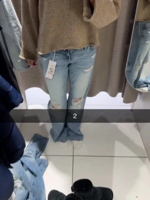 Ljusblå slitna bootcut jeans - Säljer ett par ljusblå bootcut jeans med slitningar och hål på låren och knäna. Jeansen har råa kanter vid bensluten och en avslappnad passform. Perfekta för en trendig och avslappnad look.