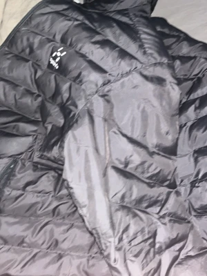 Svart dunjacka från Haglöfs - Säljer en svart dunjacka från Haglöfs med quiltad design och hög krage. Jackan har dragkedja och är tillverkad i ett glansigt material som håller värmen under kalla dagar. Perfekt för vintern och enkel att matcha med olika outfits. Använd knappt använd typ 2-3 gånger så i riktigt gott skick 900 Elr 750 möts kontant i Malmö 