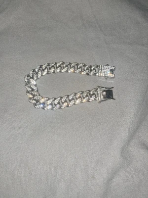 Silverfärgat kedjearmband med diamanter  - Snyggt armband i silverfärg med bred kedja och glittrande stenar på varje länk. Armbandet har ett robust spänne och ger en lyxig känsla. Perfekt för dig som gillar att sticka ut med accessoarer.