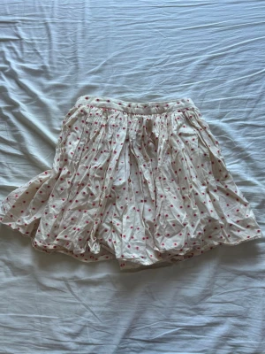 Vit prickig kjol från Topshop - Söt kortkjol från Topshop i vit bomullsblandning med röda prickar. Kjolen har en luftig och volangig form. 