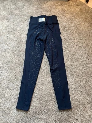 Equito Equestrian tights - Snygga marinblå tights från Equito Equestrian i storlek XS. Byxorna har medel midja, helskodda samt en metallfärgad logga bak. Endast använt ett fåtal gånger. 