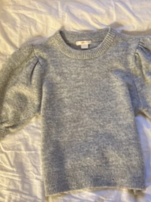 Ljusgrå stickad tröja Gina Tricot - Supermjuk ljusgrå stickad tröja från Gina Tricot med puffärmar och ribbade muddar vid hals, ärmslut och nederkant. Perfekt för lager-på-lager och enkel att matcha med jeans eller kjol. Klassisk rund halsringning och avslappnad passform.