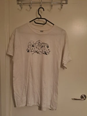 Vit t-shirt med graffiti-tryck - Vit t-shirt med svart graffiti-tryck på bröstet och mindre tryck i nacken. Hittar inga defekter.