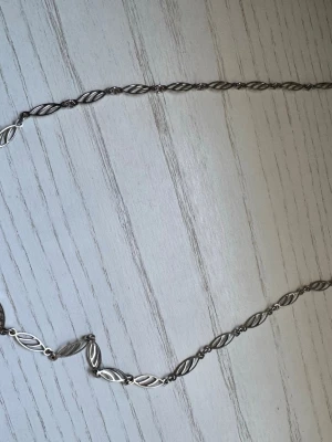 Snyggt silverfärgat halsband med tvinnad design - Unikt halsband i silverfärg med tvinnade, bladformade länkar som ger en cool och stilren look. Perfekt accessoar för att lyfta din outfit med en modern touch. Materialet är metall och designen är elegant och tidlös.