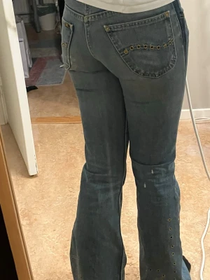 Vintage bootcut jeans med snygga detaljer - Säljer ett par blå bootcut jeans med jätte fina detaljer längs benen och på bakfickan. Jeansen har en klassisk femficksmodell och är tillverkade i denim med lätt tvättad look. Jeansen är i topp skick och är tillverkade vid ca 70-tal. Storleken är 28/33 men är ca 85 i innerbensmått och ca 40cm i midjan tvärs över. Hör av dig vid frågor 🤗