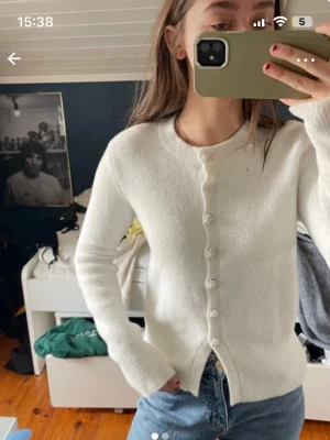 Vit kofta med pärlknappar - Säljer en stilren vit kofta med rund halsringning och dekorativa pärlknappar framtill. Koftan har lång ärm och är gjord i ett mjukt stickat material som känns skönt mot huden. Perfekt att matcha med jeans för en enkel look.