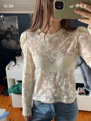 Vit spetsblus med puffärm - Säljer en vit spetsblus med långärmad design och puffade axlar. Blusen är genomskinlig med ett vackert spetsmönster och rund halsringning. Perfekt att styla med jeans eller kjol för en trendig look.