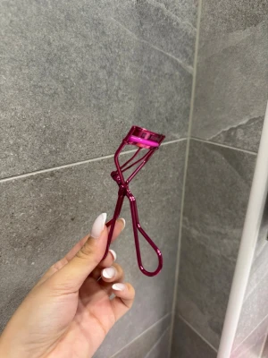 Rosa ögonfransböjare Real Techniques - Snygg ögonfransböjare från Real Techniques i metallicrosa färg. Den har en klassisk böjd form och är tillverkad i metall med ett greppvänligt handtag. Perfekt för att lyfta och forma fransarna snabbt och enkelt.