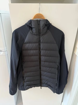 Svart dunjacka från Moncler - Snygg svart dunjacka från Moncler med huva och dragkedja framtill. Jackan har quiltad design på fram- och baksidan samt släta ärmar. Två fickor med dragkedja och diskret Moncler-logga på ärmen. Perfekt för kalla dagar. Diskret och snygg för den som vill sticka ut med en unik Moncler jacka. Priset går att diskutera. Size 3 som motsvarar Large.