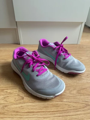 Grå Nike sneakers med lila detaljer - Snygga sneakers från Nike i grå mesh med turkos swoosh och lila detaljer. Skorna har lila snören och foder, samt vit sula med lila inslag undertill. Perfekta för träning eller en sportig look