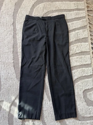 Svarta raka kostymbyxor - Klassiska svarta kostymbyxor med rak passform och pressveck. Byxorna har hällor för bälte, två sidofickor fram och två passpoalfickor bak. Storlek L/52. Knappt använda. 