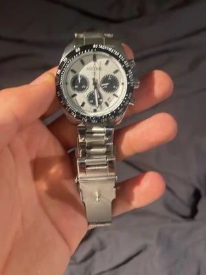 Silverfärgad Seiko kronografklocka - Stilren Seiko kronografklocka i silver med metallarmband och vit urtavla. Klockan har svarta detaljer, tre subdials och tachymeter på bezeln. Perfekt accessoar för dig som gillar klassisk och sportig stil.