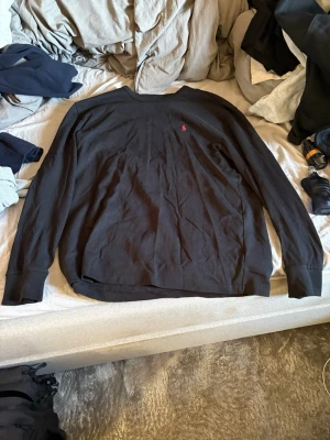 Svart långärmad tröja Polo Ralph Lauren - Svart långärmad tröja från Polo Ralph Lauren i klassisk passform. Tröjan har rund halsringning och den ikoniska röda Polo-loggan broderad på bröstet. Tillverkad i mjukt bomullsmaterial som är skönt mot huden.