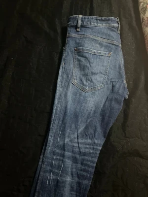 Blå Dsquared2 jeans med rosdetalj  - Säljer ett par blå jeans från Dsquared2 med snygg tvätt och en unik patch bak med rosor och Dsquared2-logga. Klassisk femficksmodell och raka ben. Perfekta för dig som vill ha något extra i garderoben. Jag har mer bilder men går inte att lägga mer än 7 behöver du mer skickar jag 